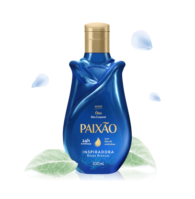 Paixão Inspiradora Rosas Brancas Körperöl mit Mandelöl, blaue Flasche mit goldenem Verschluss, umgeben von grünen Blättern und hellen Blütenblättern
